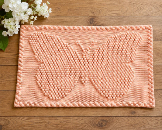 Free small butterfly baby blanket crochet pattern in peach with bobble stitch butterfly motif on a wooden floor with white flowers