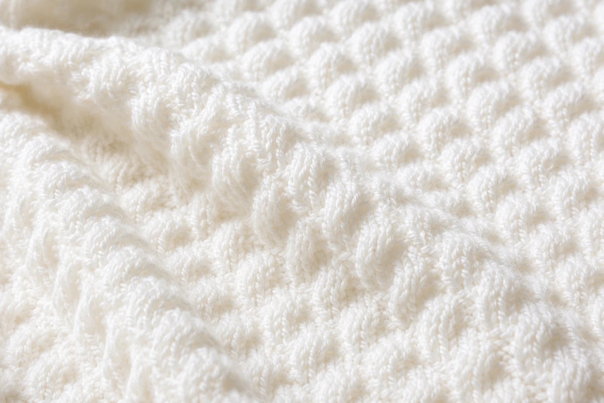 Elegant close up of the white Diagonal Bumps baby blanket showing the textured knitted stitch pattern and soft folds