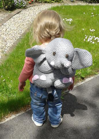 Toddler wearing elephant backpack crochet pattern in a garden showing the finished animal backpack design