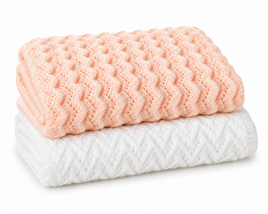 Two folded textured Lace Baby Blankets, one peach and one white, on a white background