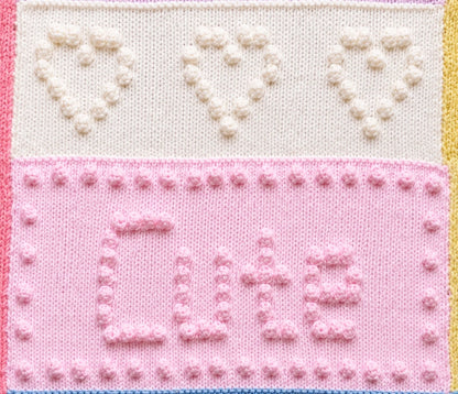 Close-up of the Sweet Dreams baby blanket showing bobble stitch hearts and the Cute word panel knitted using knit, purl and bobble stitches.