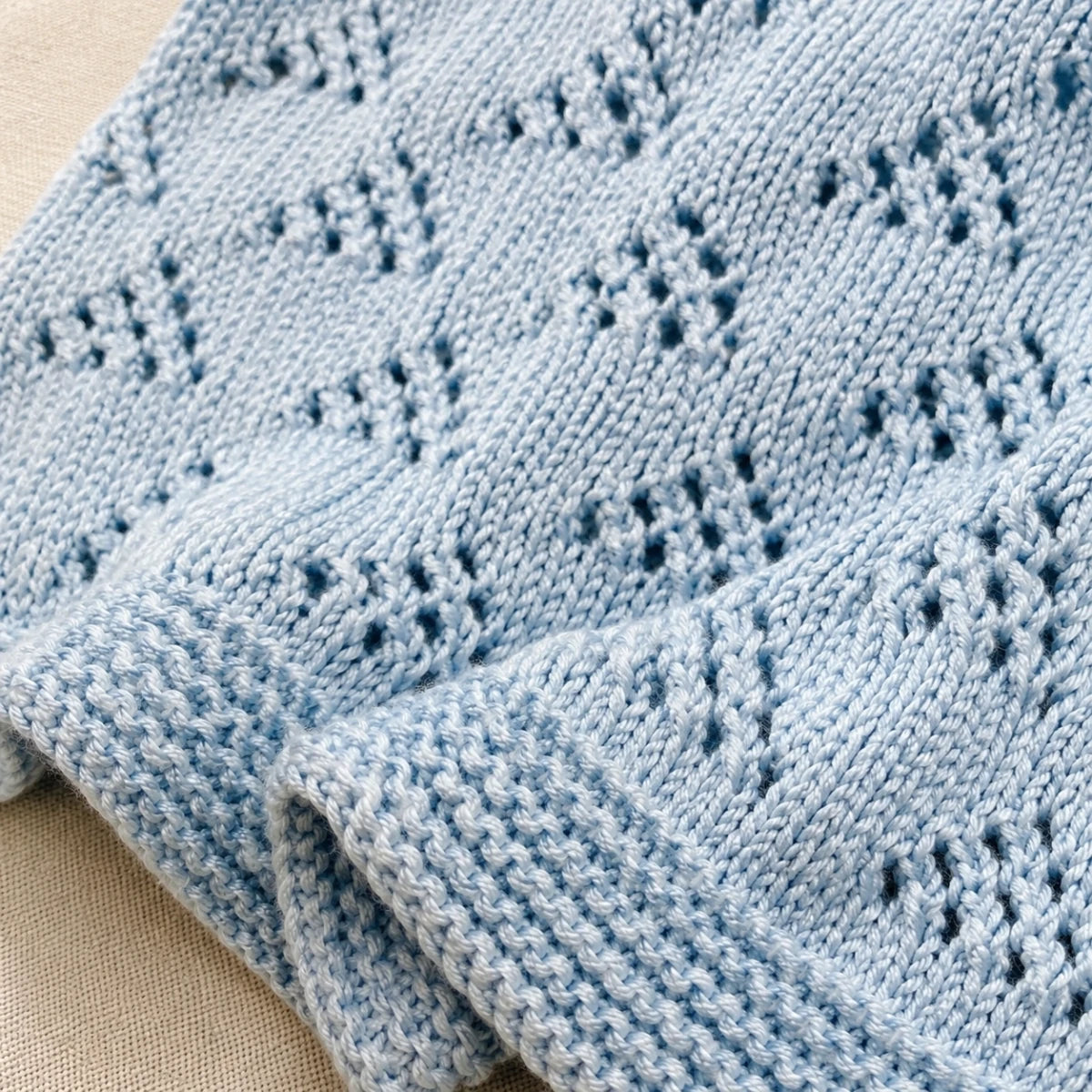 Close-up texture of blue lace baby blanket knitting pattern with delicate eyelet stitch detail and garter stitch border