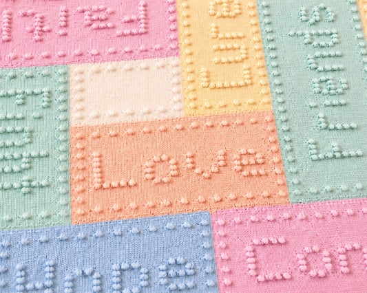 Close up of pastel cancer support lap blanket knitting pattern showing textured words and bobble stitch border detail in soft pink, blue, mint and peach panels.