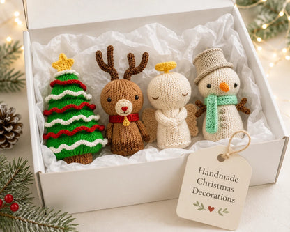 Handmade Christmas decorations gift box featuring knitted Christmas tree, reindeer, angel and snowman displayed in white tissue paper.