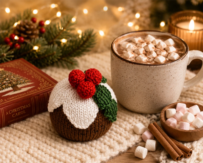 Handmade knitted Christmas pudding decoration beside hot chocolate, marshmallows and fairy lights in a cosy festive Christmas scene for a free worked flat knitting pattern