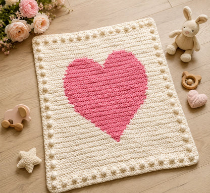 Chunky Intarsia Heart crochet blanket displayed on a wooden nursery floor with soft flowers and baby toys.