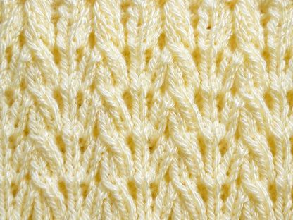 Elegant close up of the Corn Rows baby blanket knitting pattern showing soft pastel yellow textured knit stitches with repeating raised cable-style rows and delicate vertical detail