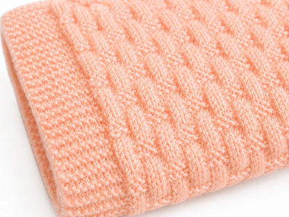 Close up of the Cosy Weaving baby blanket knitting pattern showing textured knit and purl stitch detail in soft peach yarn