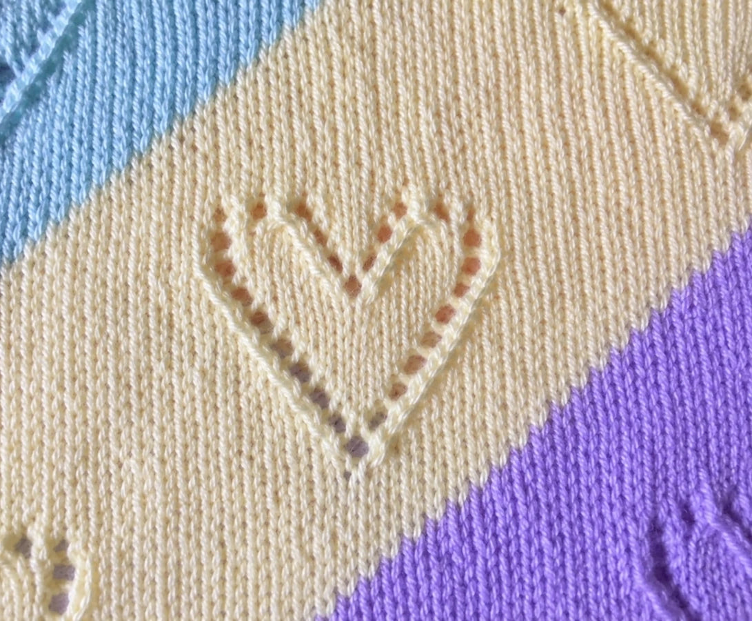 Close up of Diagonal Lace baby blanket knitting pattern showing pastel diagonal stripes with delicate lace heart stitch detail and soft knitted texture