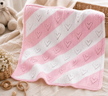 laid out pink and white diagonal lace baby blanket knitting pattern with heart eyelet design in cosy nursery scene