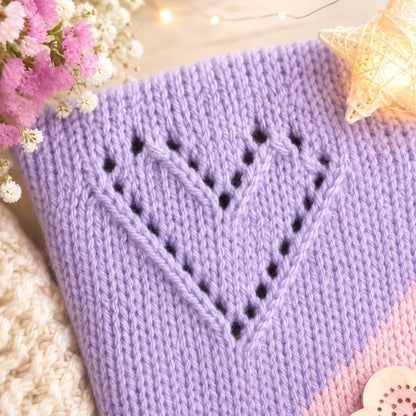 Close up of pastel purple diagonal lace heart stitch knitting pattern with soft nursery styling, fairy lights and floral details for baby blanket inspiration