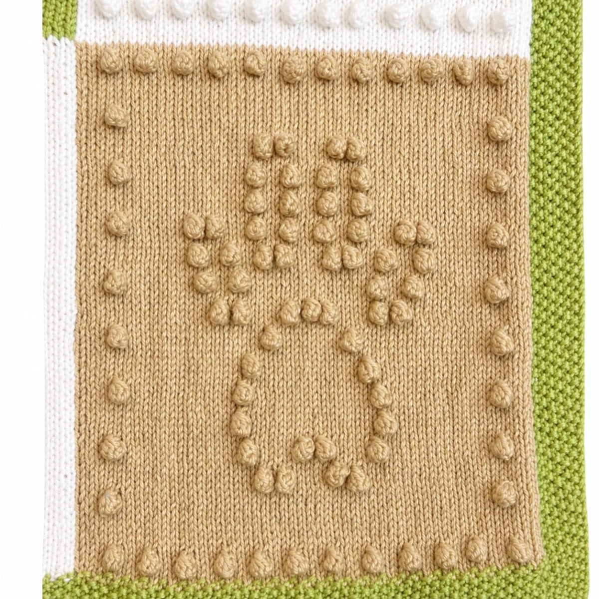 Close-up texture detail of the Dog Life baby blanket knitting pattern showing raised bobble stitch paw print motif with green, cream and beige knitted sections.