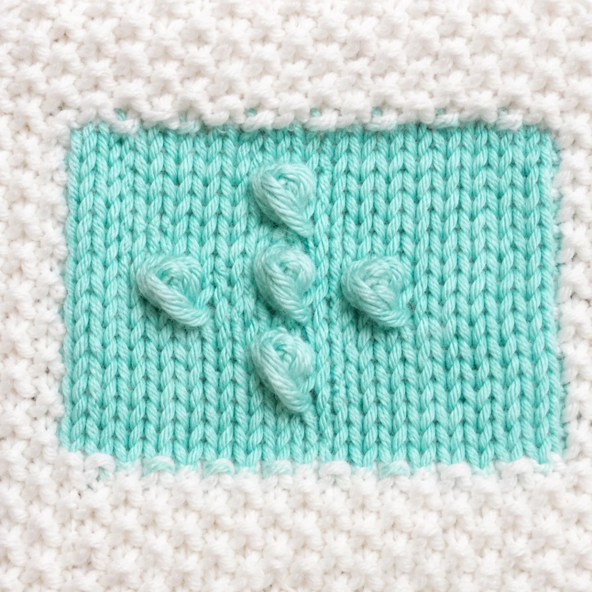 Close-up of mint intarsia colourwork square showing raised bobble stitches, stockinette texture and white seed stitch border