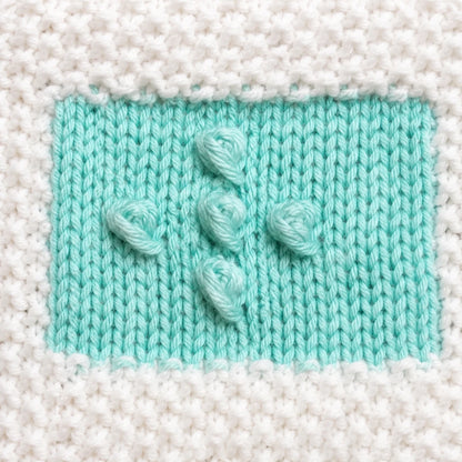 Close-up texture image of free knitting practice pattern showing bobble stitch detail, neat intarsia colour joins, stockinette stitch texture, and seed stitch border for beginner knitting practice.