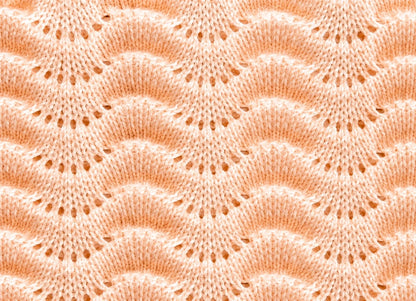 Close up texture detail of the Gentle Waves baby blanket knitting pattern in soft peach yarn showing the repeating scalloped lace wave stitch design.