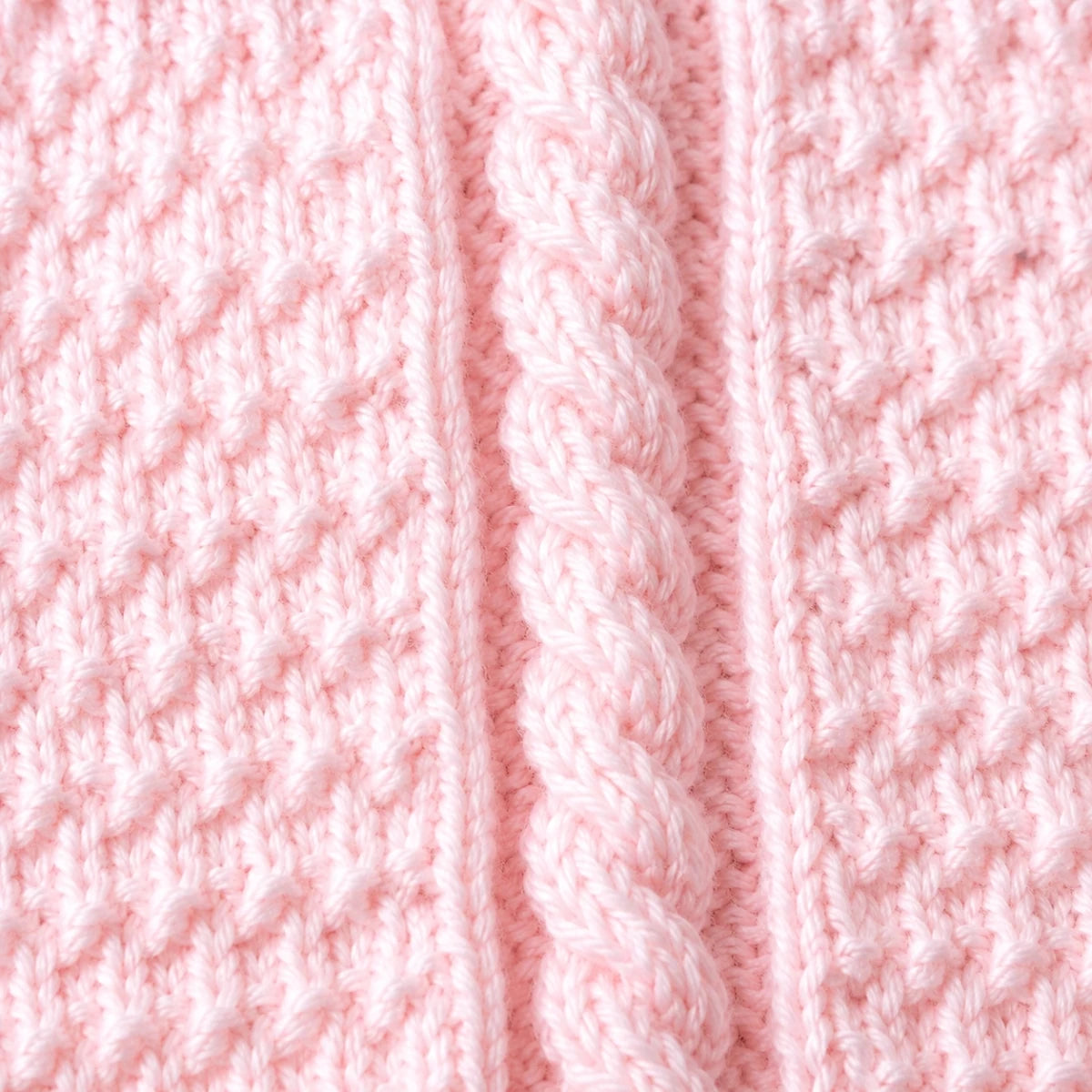 Close-up of a soft-pink Granite Cable baby blanket showing raised cable twists and textured knitted panels