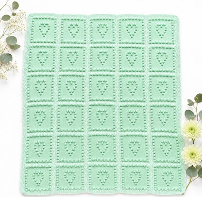 Heart Squares baby blanket knitting pattern in soft mint green tones with textured bobble heart squares on a white background with delicate complementary flowers and soft natural styling