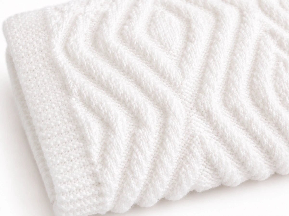 Close up of the Hidden Crosses baby blanket knitting pattern showing textured knit and purl stitch detail in soft white yarn