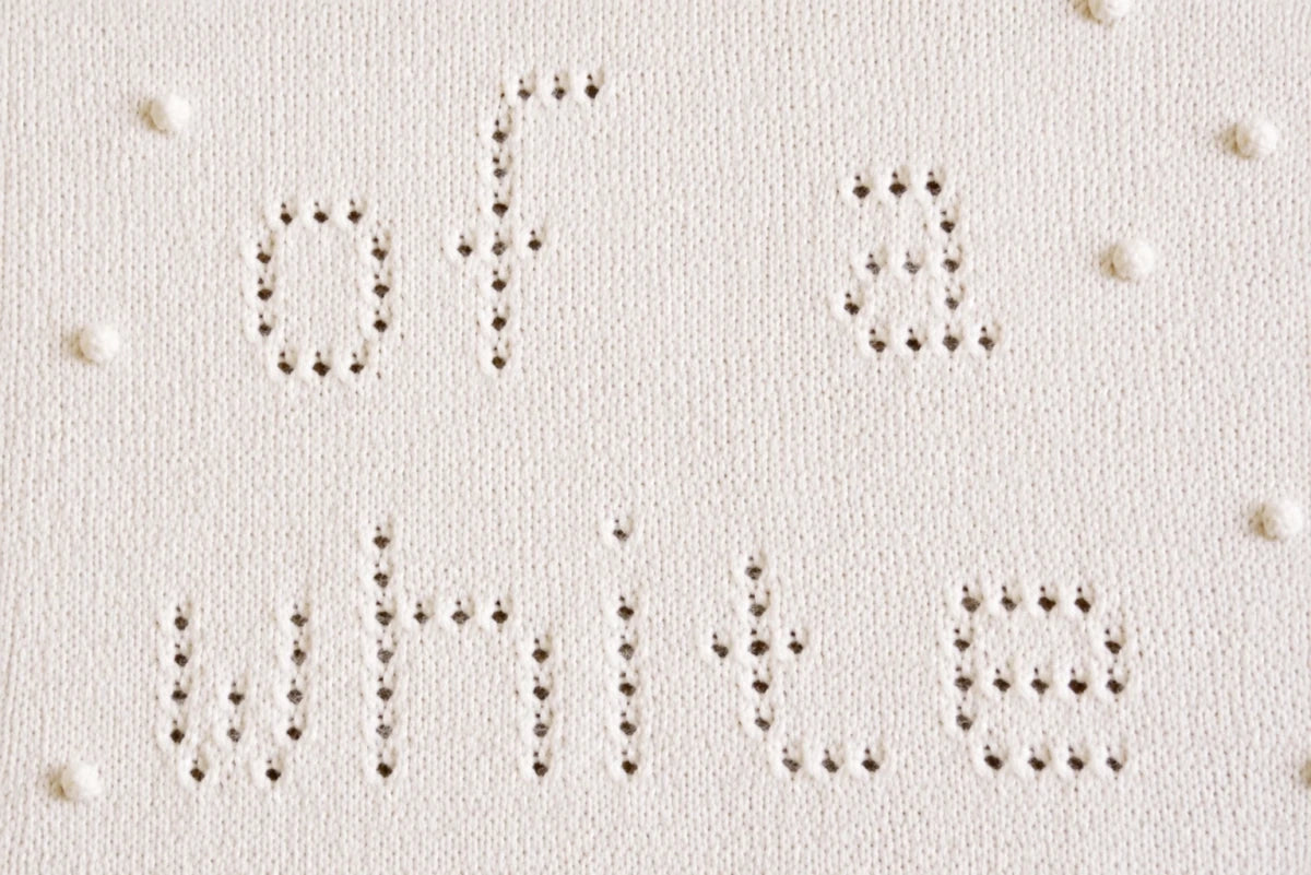 Close-up of the lace knitting detail from the I'm Dreaming of a White Christmas baby blanket knitting pattern showing eyelet lettering and textured bobble accents.