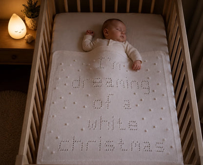 Sleeping baby covered with I'm Dreaming of a White Christmas baby blanket knitting pattern in a cosy nursery at night