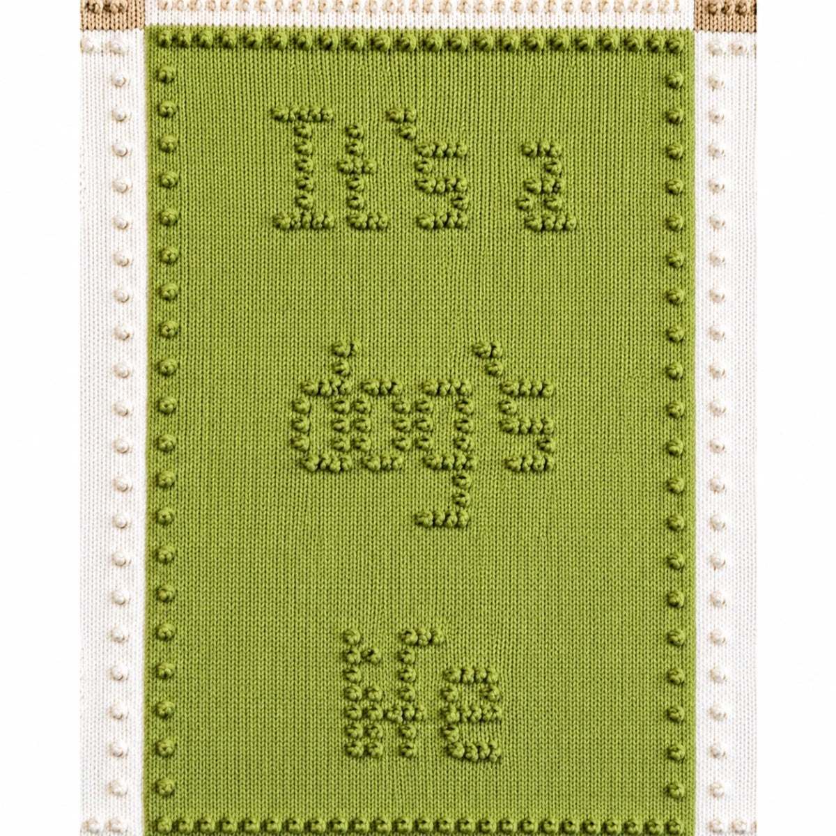 Close-up of green “It’s a dog’s life” panel on a knitted dog blanket featuring bobble stitch lettering and cream textured borders