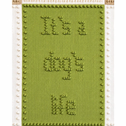Close-up of green “It’s a dog’s life” panel on a knitted dog blanket featuring bobble stitch lettering and cream textured borders
