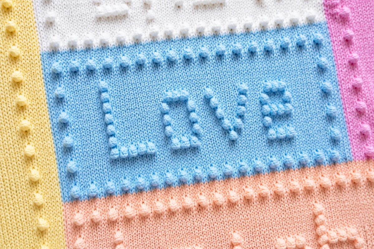 Close-up of the Love panel on the Joy baby blanket knitting pattern featuring pastel intarsia colour blocks and raised bobble lettering