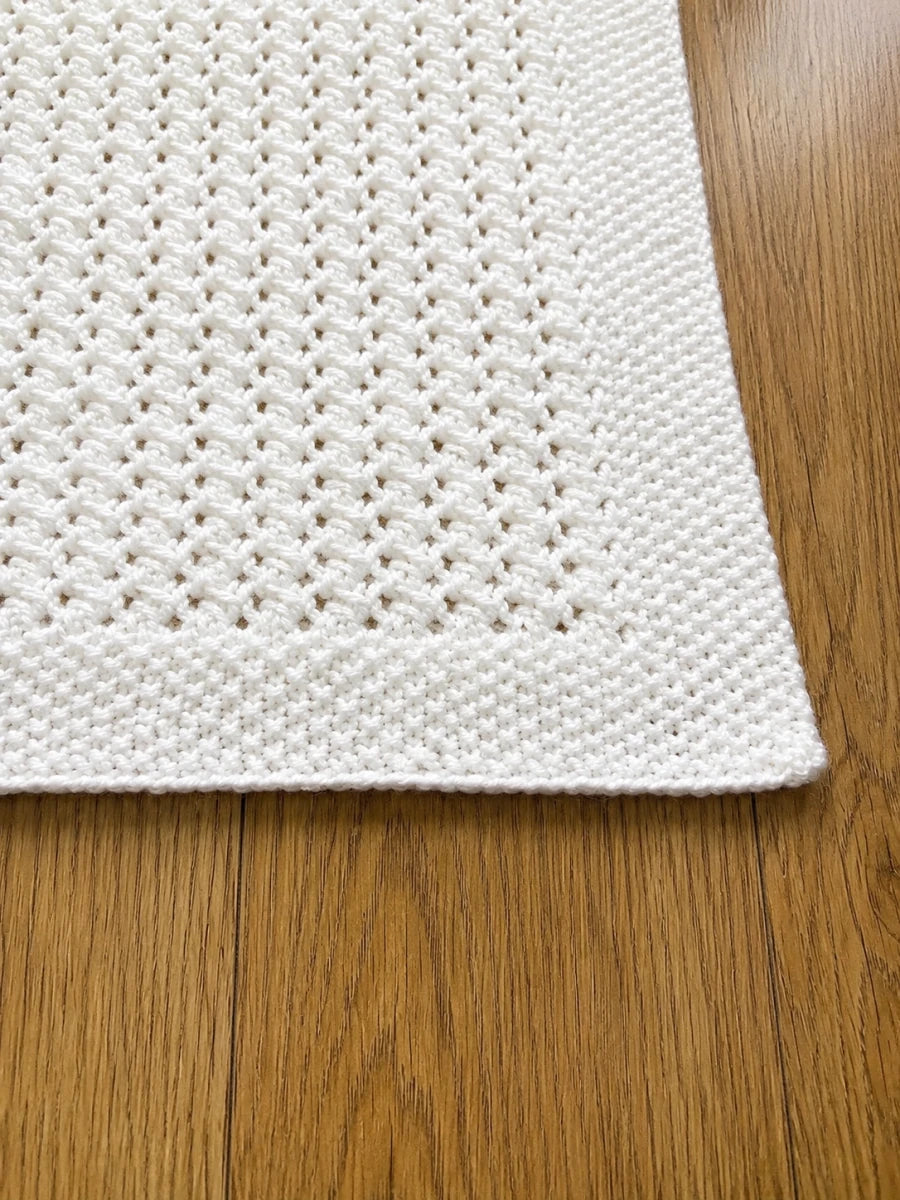 Close up of the white Lattice Love baby blanket showing the slipped stitch texture and neat seed stitch border