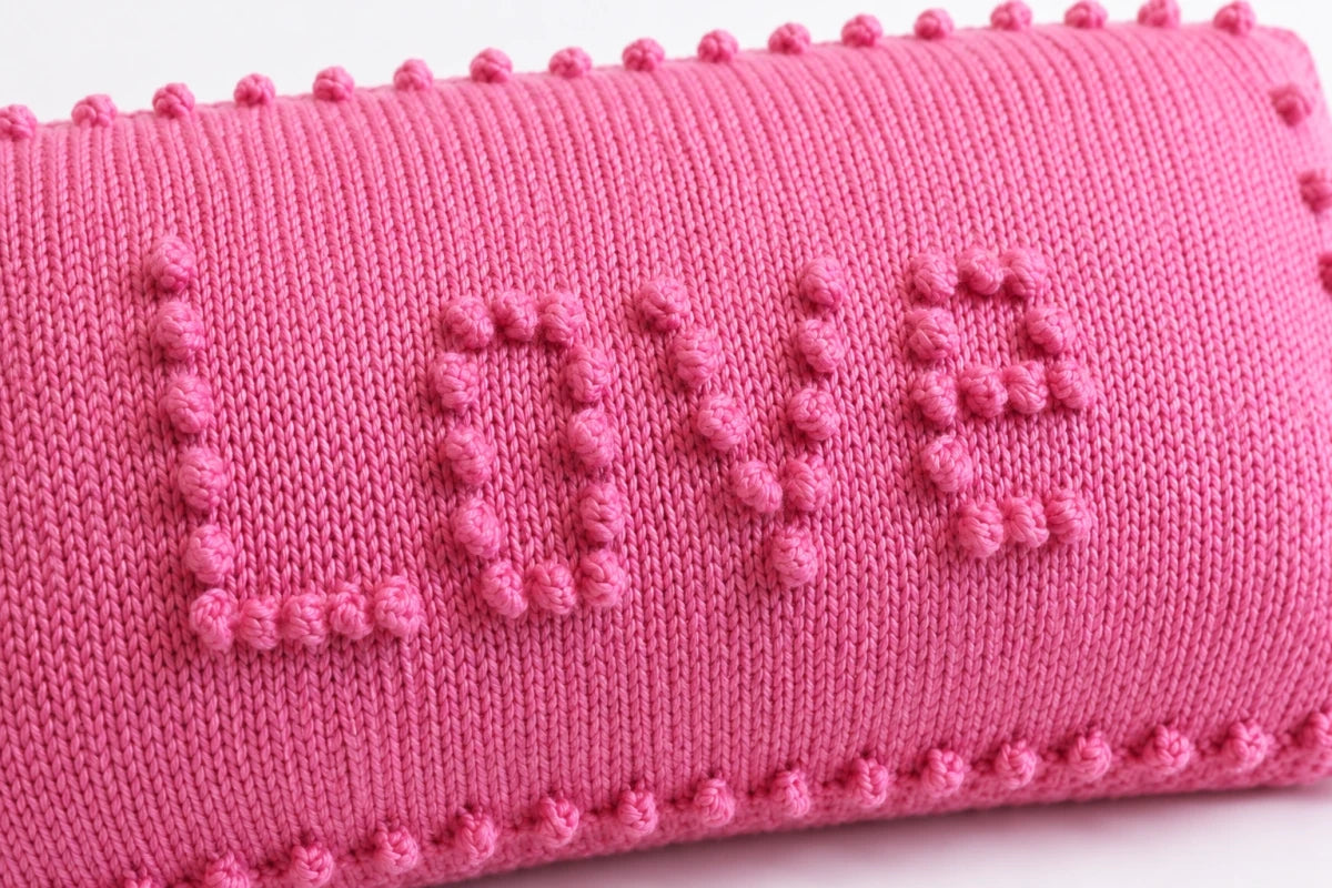 Close-up of pink LOVE pillow knitting pattern showing raised bobble stitch lettering, smooth stockinette stitch fabric and decorative bobble border