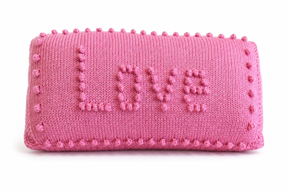 Pink LOVE pillow knitting pattern featuring bobble stitch lettering, stockinette stitch panels and decorative bobble border on a cushion cover