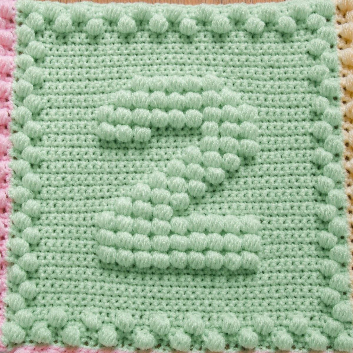 Close-up of a mint green crochet motif featuring a raised puff stitch number two.