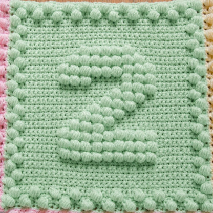 Close-up of a mint green crochet motif featuring a raised puff stitch number two.