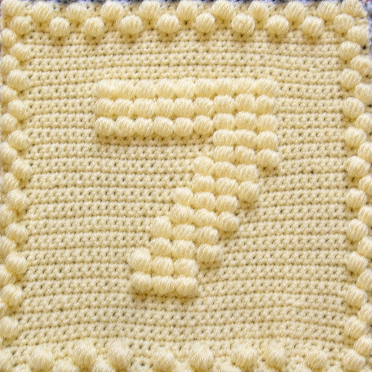 Close-up of a pale yellow crochet motif featuring a raised puff stitch number seven.