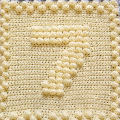 Close-up of a pale yellow crochet motif featuring a raised puff stitch number seven.