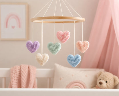Pastel knitted heart mobile hanging above baby cot in soft nursery
