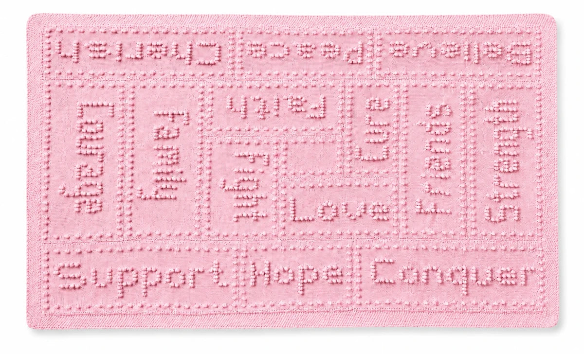 Soft pastel pink knitted cancer support lap blanket with comforting words and textured bobble stitch panels on a white background