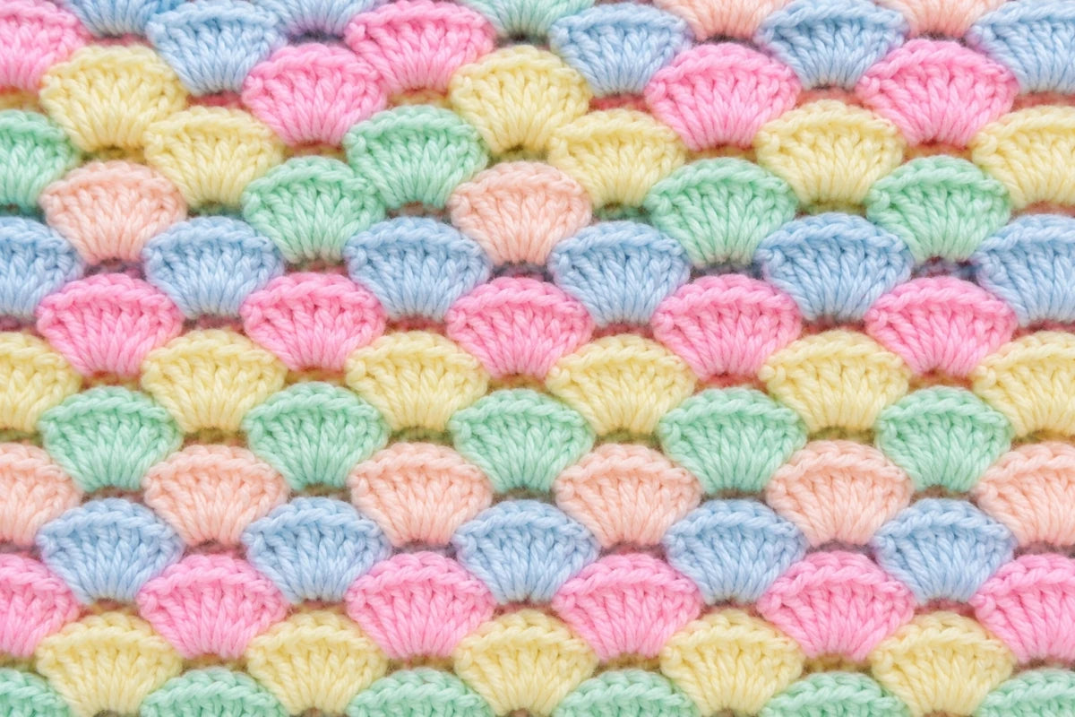 Close up of the Pastel Shells crochet baby blanket showing pastel shell stitch texture with 7 double crochet stitches in each shell using pink blue peach green and yellow yarn colours