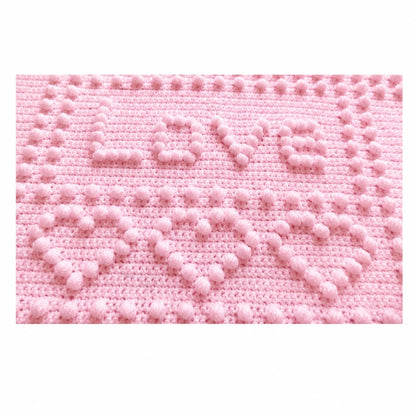 Close-up of the Love panel and puff stitch hearts on the soft pink Precious One-Piece Baby Blanket crochet pattern.