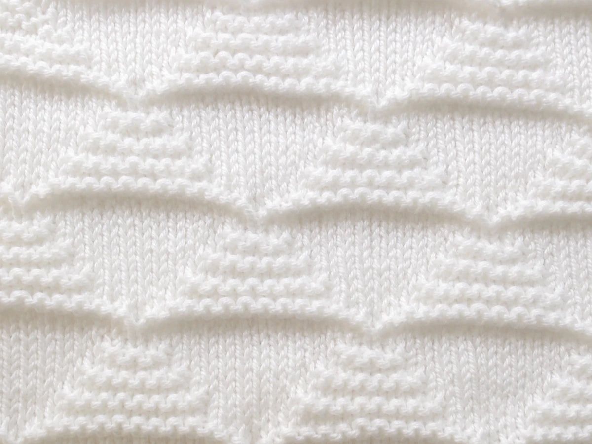 Elegant close up of white Pyramids baby blanket knitting pattern showing textured knit and purl pyramid stitch detail in soft ivory yarn