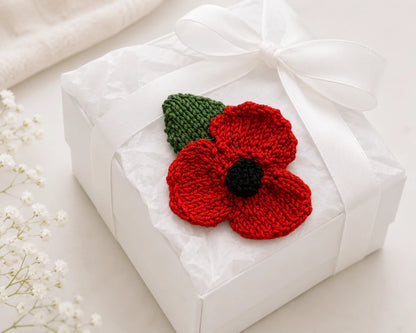 Hand knitted remembrance poppy displayed on a white gift box with ribbon and tissue paper