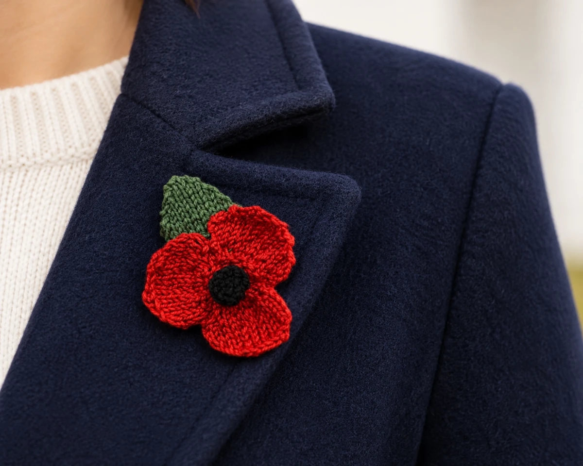 Hand knitted remembrance poppy pinned to a navy coat lapel for Remembrance Day