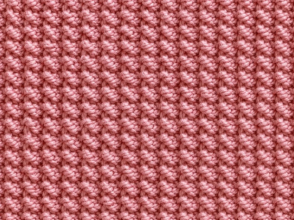 Elegant close up of a dusty rose pink rice stitch knitted baby blanket showing the soft textured stitch detail and cosy knitted fabric pattern.