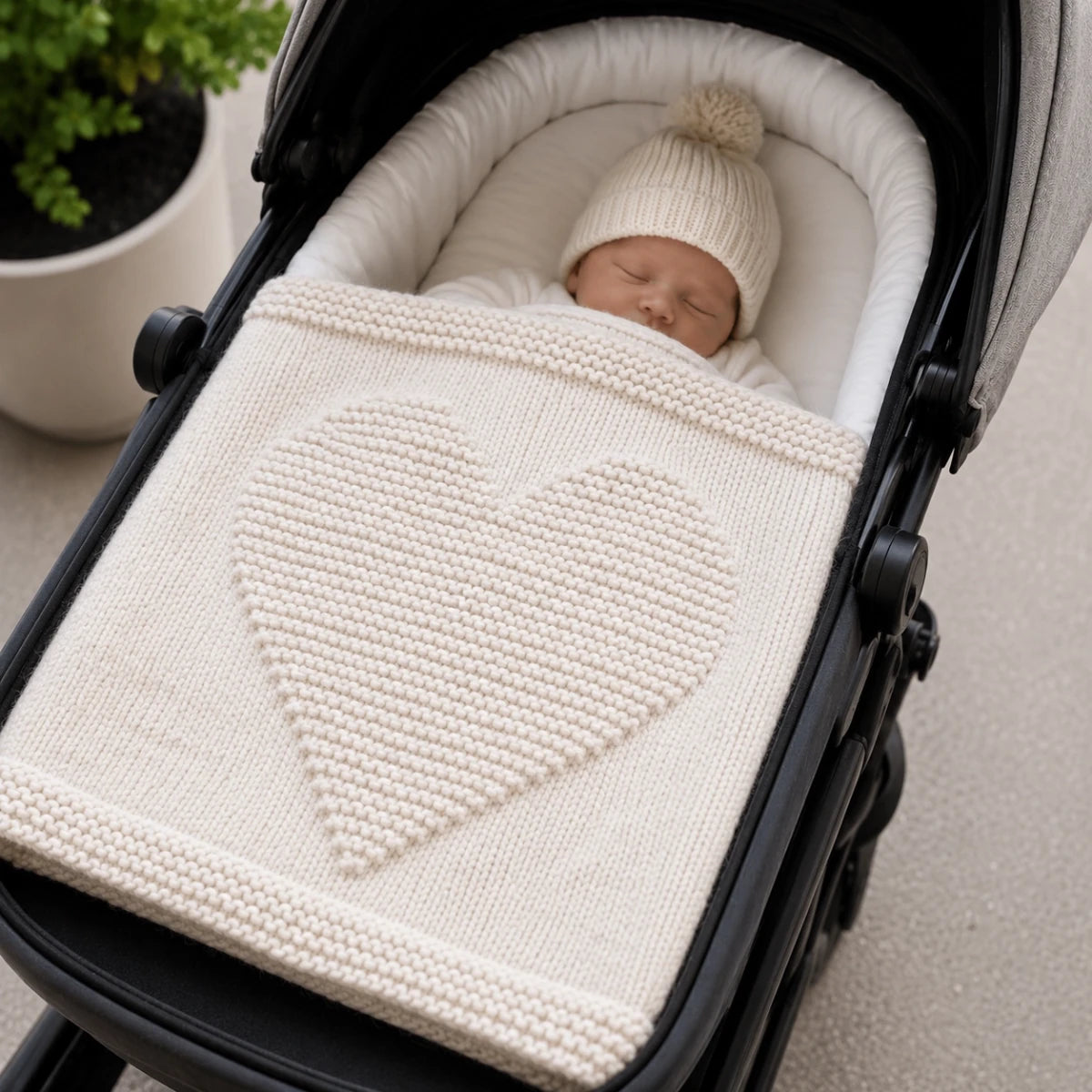 Sleeping baby in a pram covered with the Simple Chunky Heart Baby Blanket showing the raised heart design and cosy super chunky texture