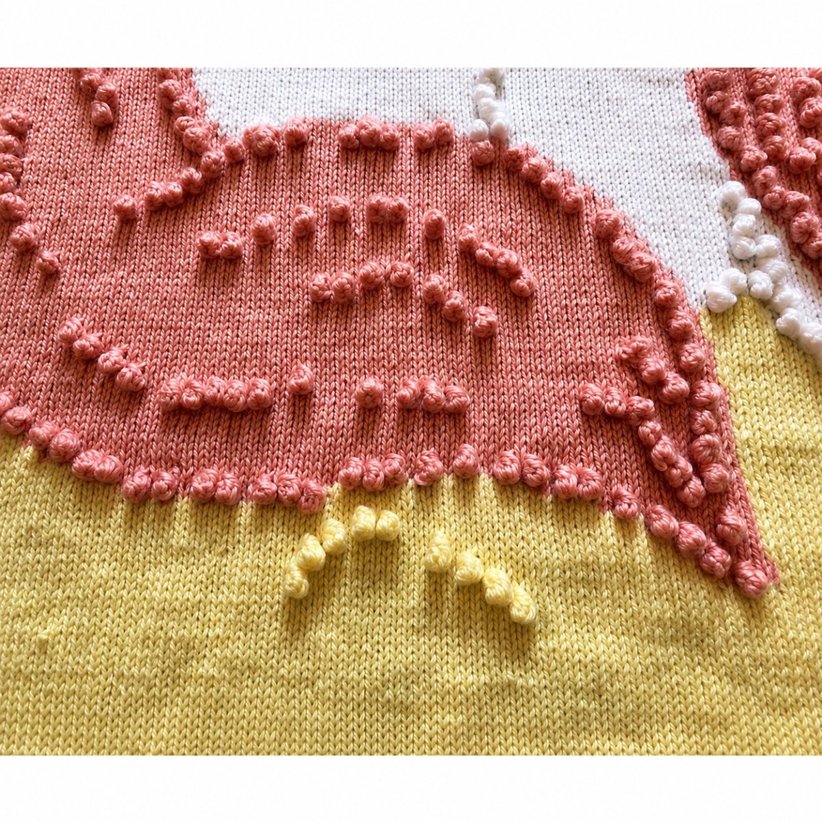 Close-up detail of the Sleeping Peach Unicorn blanket knitting pattern showing textured bobble stitches, unicorn tail and soft pastel intarsia knitting design
