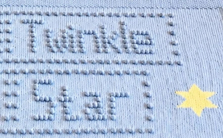 Close-up of Twinkle Twinkle Little Star knitted baby blanket showing bobble stitch lettering and intarsia star detail