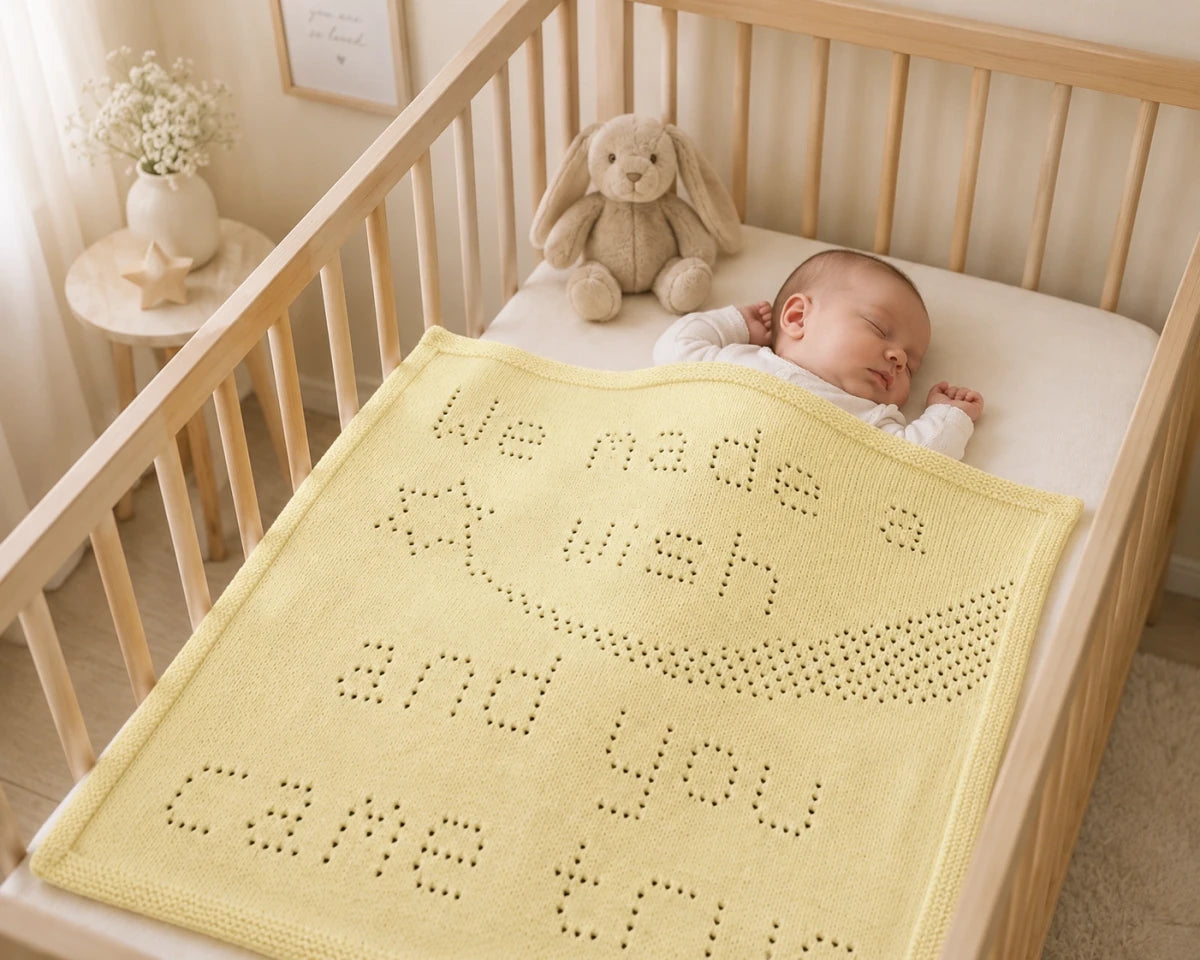 Sleeping baby in a wooden cot covered with the We Made a Wish baby blanket knitting pattern in a cream nursery