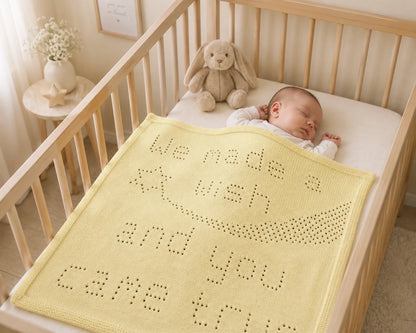 Sleeping baby in a wooden cot covered with the We Made a Wish baby blanket knitting pattern in a cream nursery