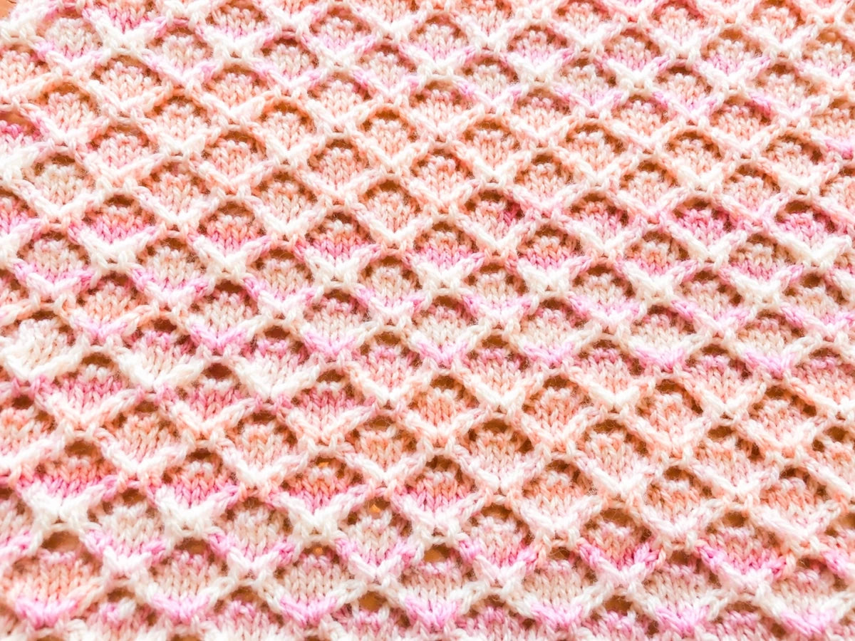 Close up texture detail of the Wiggly Curves baby blanket knitting pattern in pink variegated yarn showing the delicate lace stitch design and repeating wave pattern.
