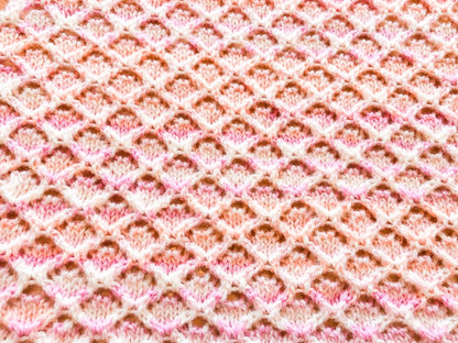 Close up texture detail of the Wiggly Curves baby blanket knitting pattern in pink variegated yarn showing the delicate lace stitch design and repeating wave pattern.