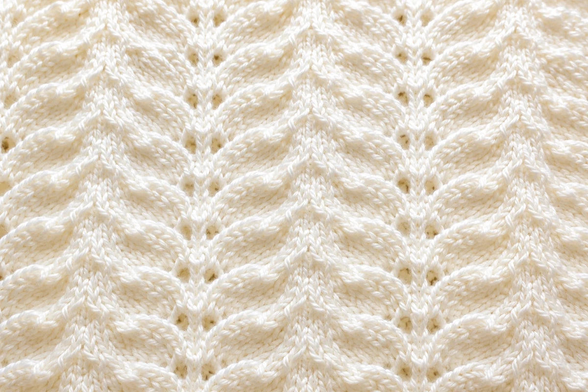 Elegant close up of antique white Wings baby blanket knitting pattern showing textured feather and lace stitch detail in soft ivory yarn